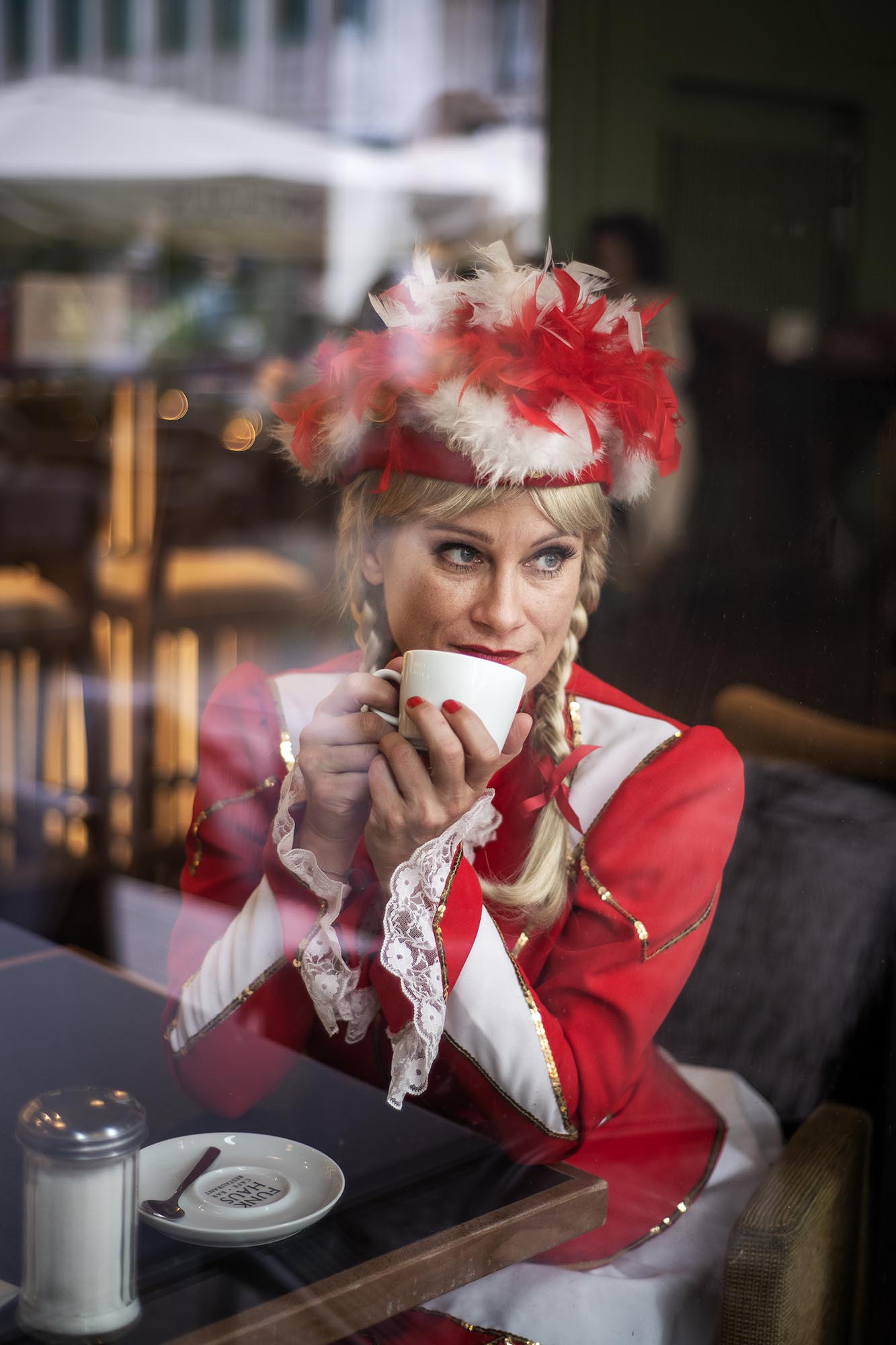 Portrait durch die Fensterscheibe fotografiert von einem blonden Tanzmariechen im Café, die nach draußen schaut.