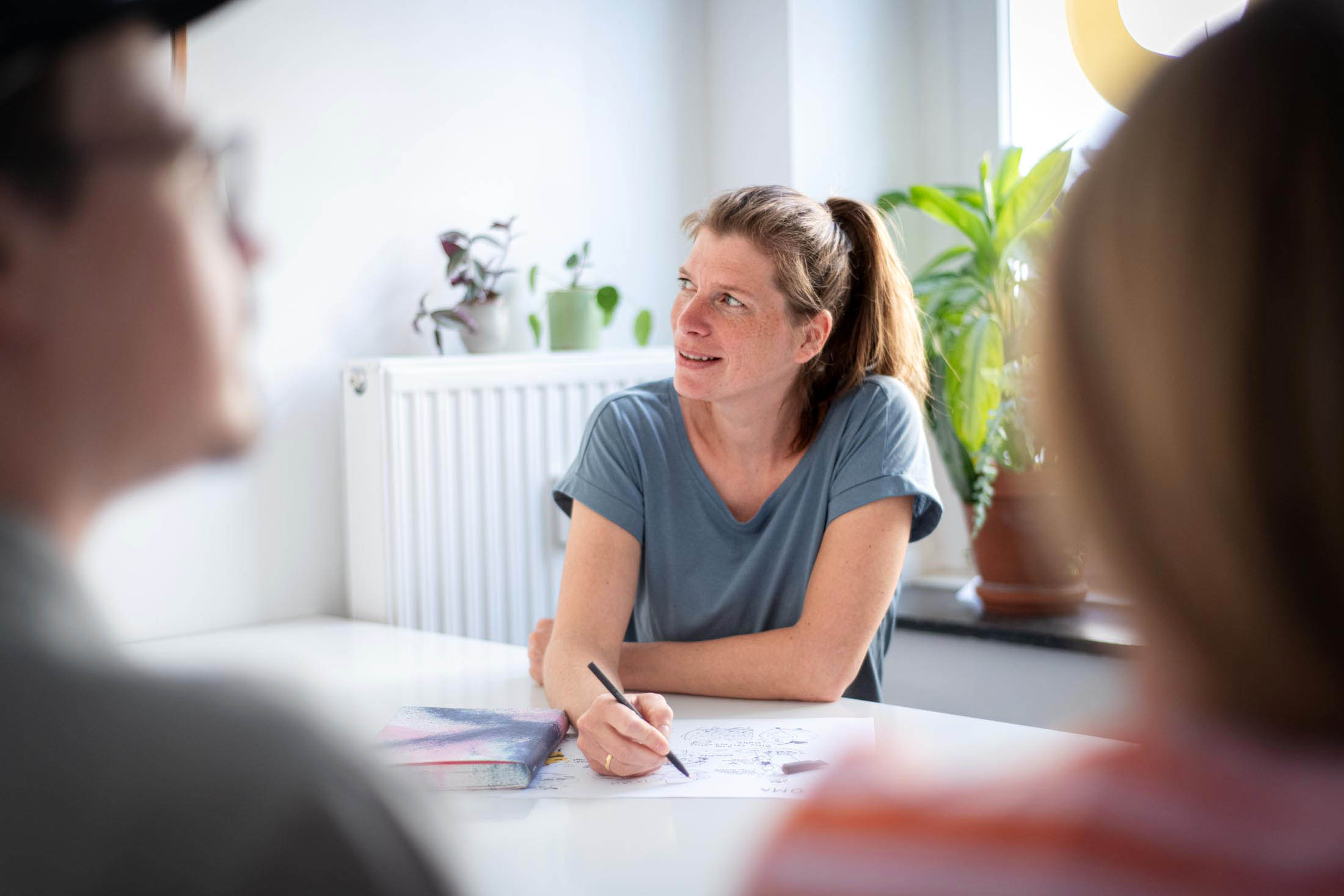 Mitarbeiterin im Meeting am Tisch, andere unscharf im Vordergrund