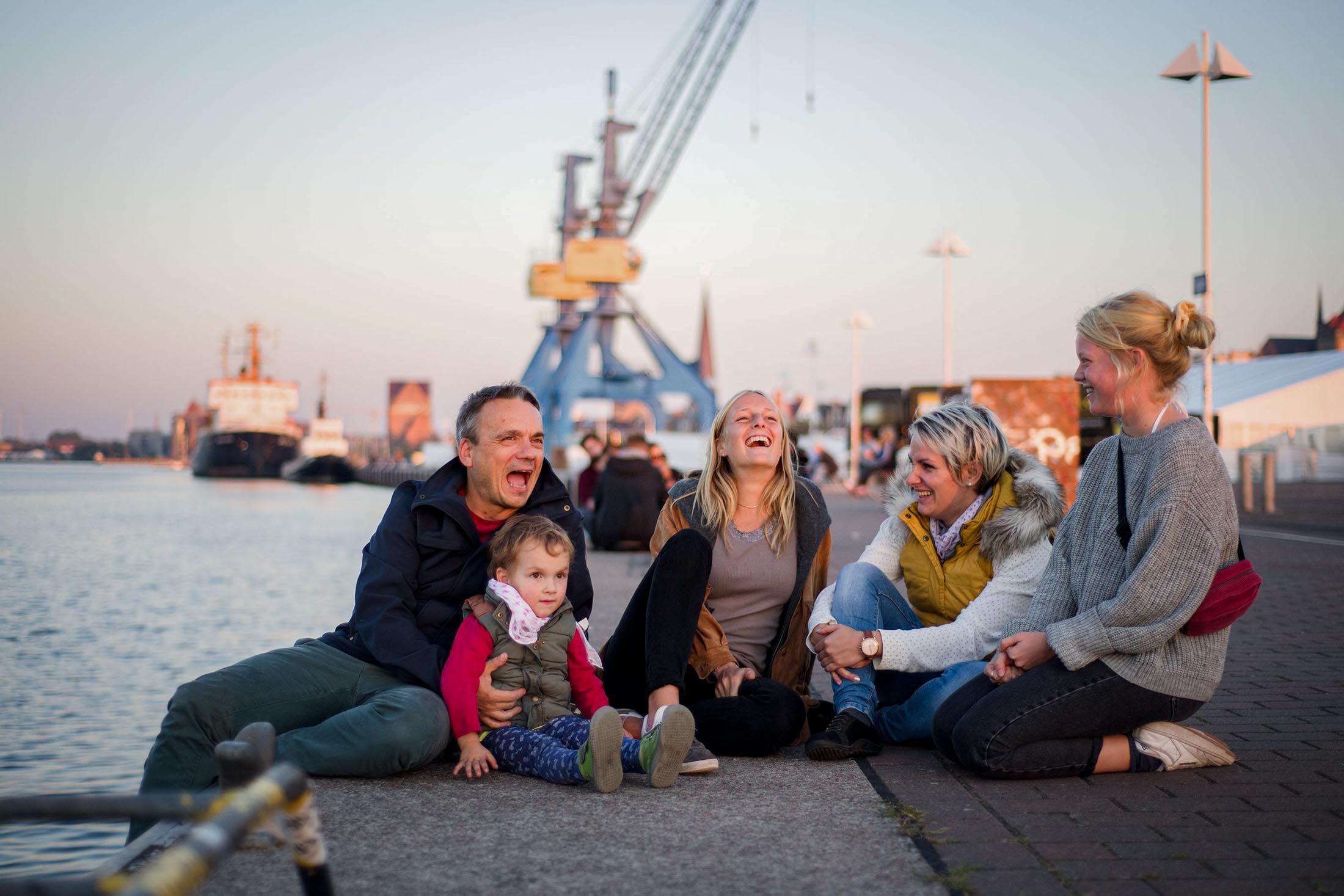 Gruppe von Menschen sitzt am Hafen auf einer Kaimauer