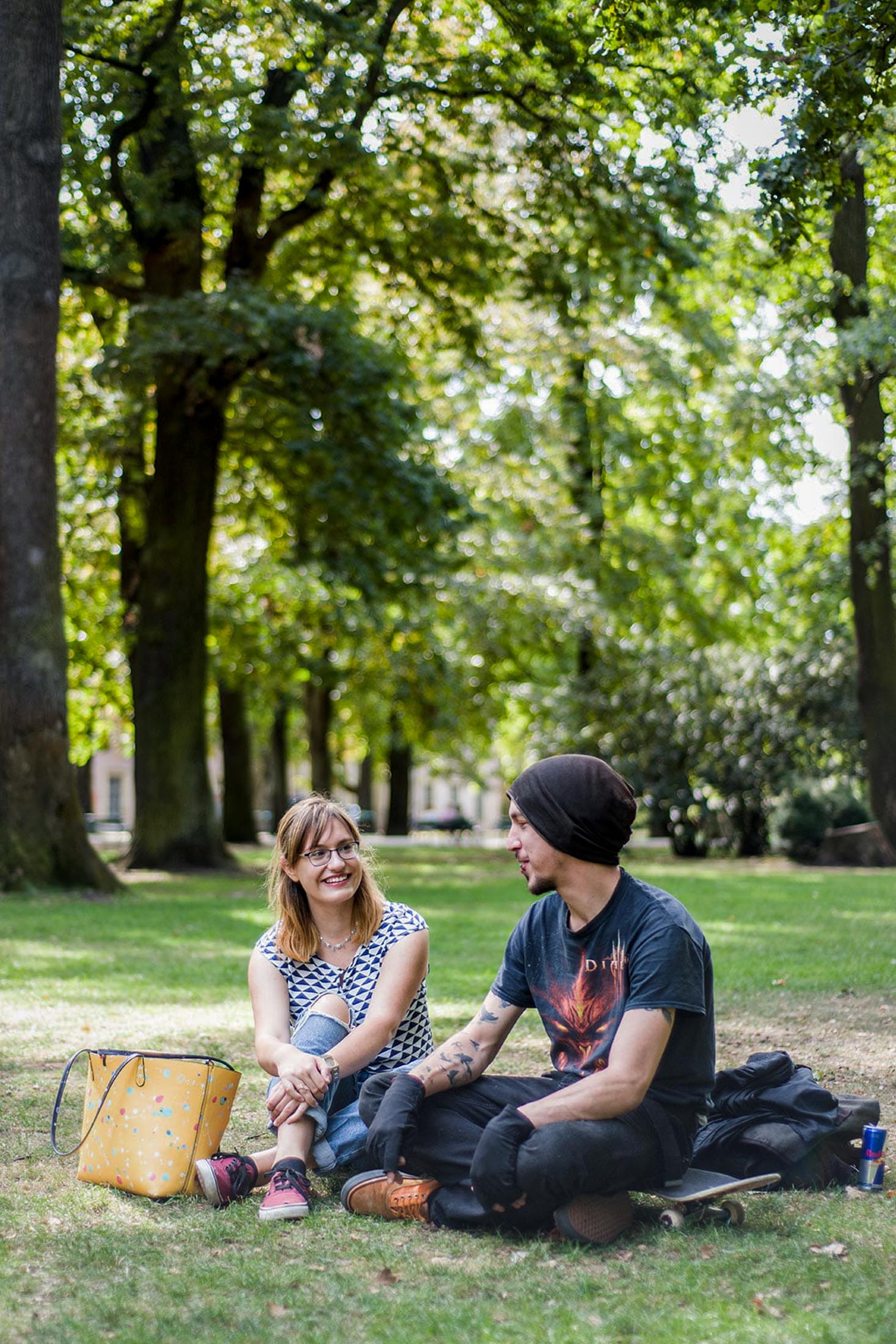Zwei junge Menschen sitzen im Park auf einer Decke und sprechen miteinander