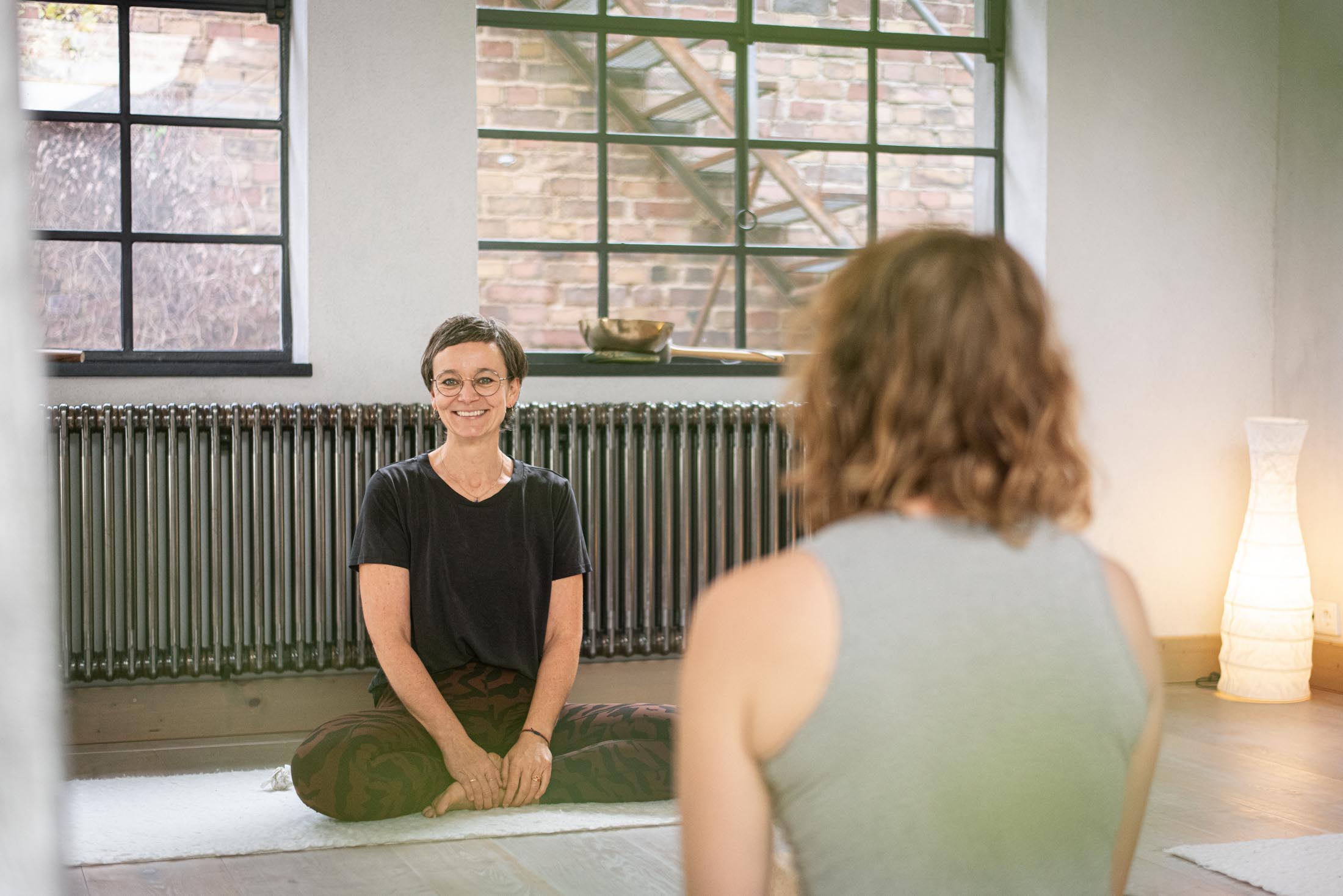 Yogalehrerin im Schneidersitz vor Kursteilnehmerinnen und lächelt in die Kamera