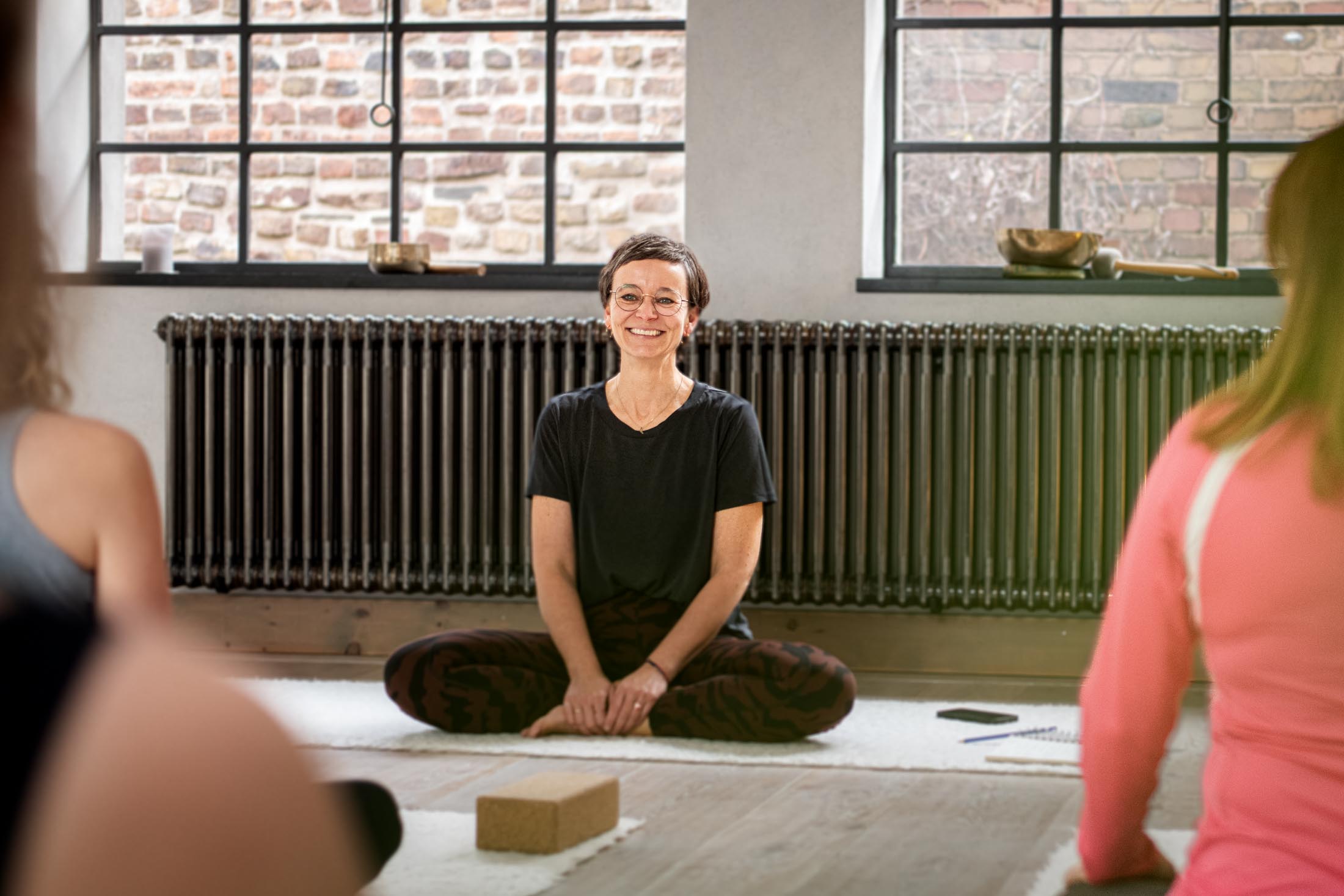 Yogalehrerin im Schneidersitz vor Kursteilnehmerinnen