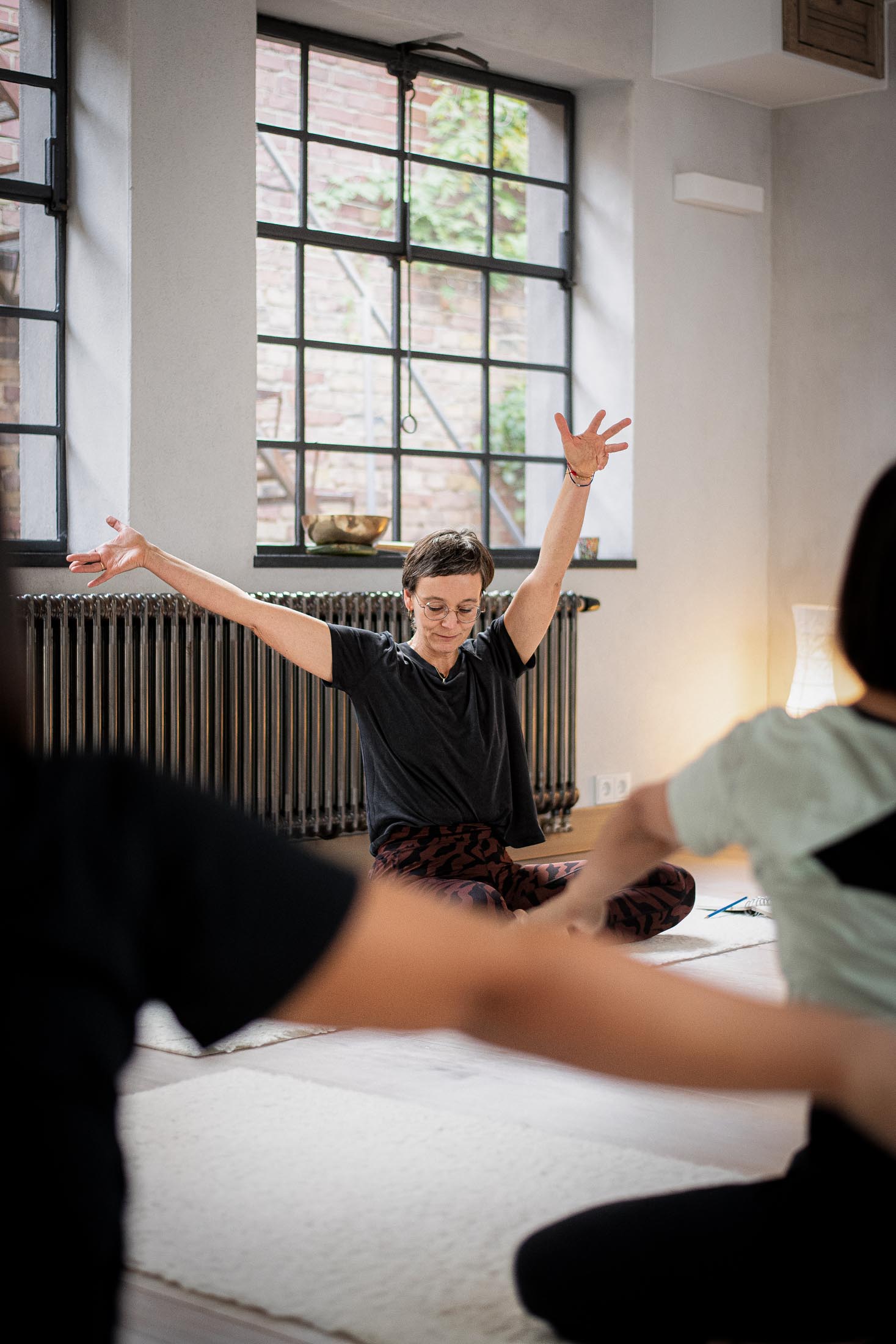 Yogalehrerin sitzt mit erhobenen Armen vor der Gruppe