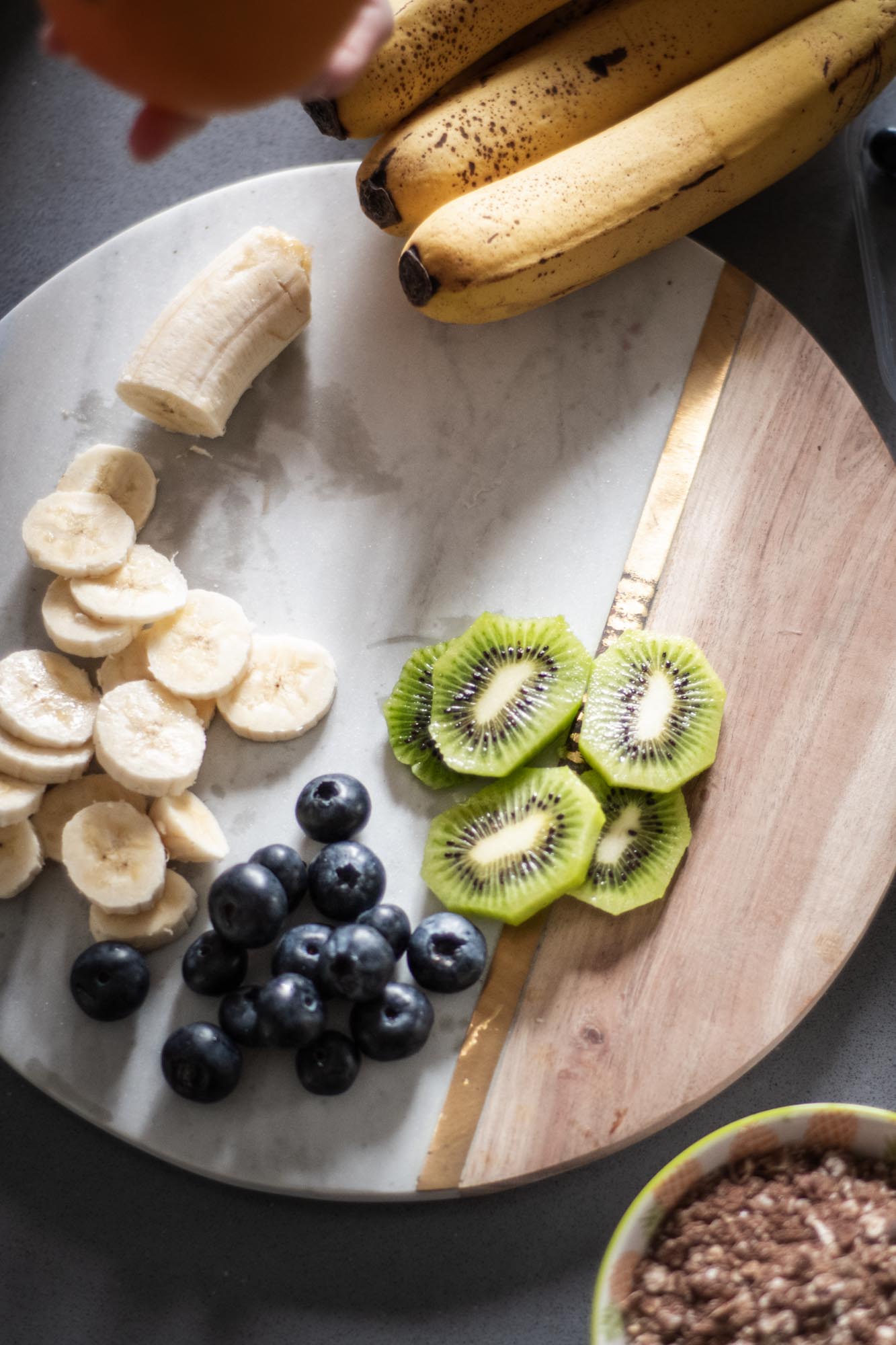 Schneidebrett mit geschnittener Banane, Kiwi und Heidelbeeren