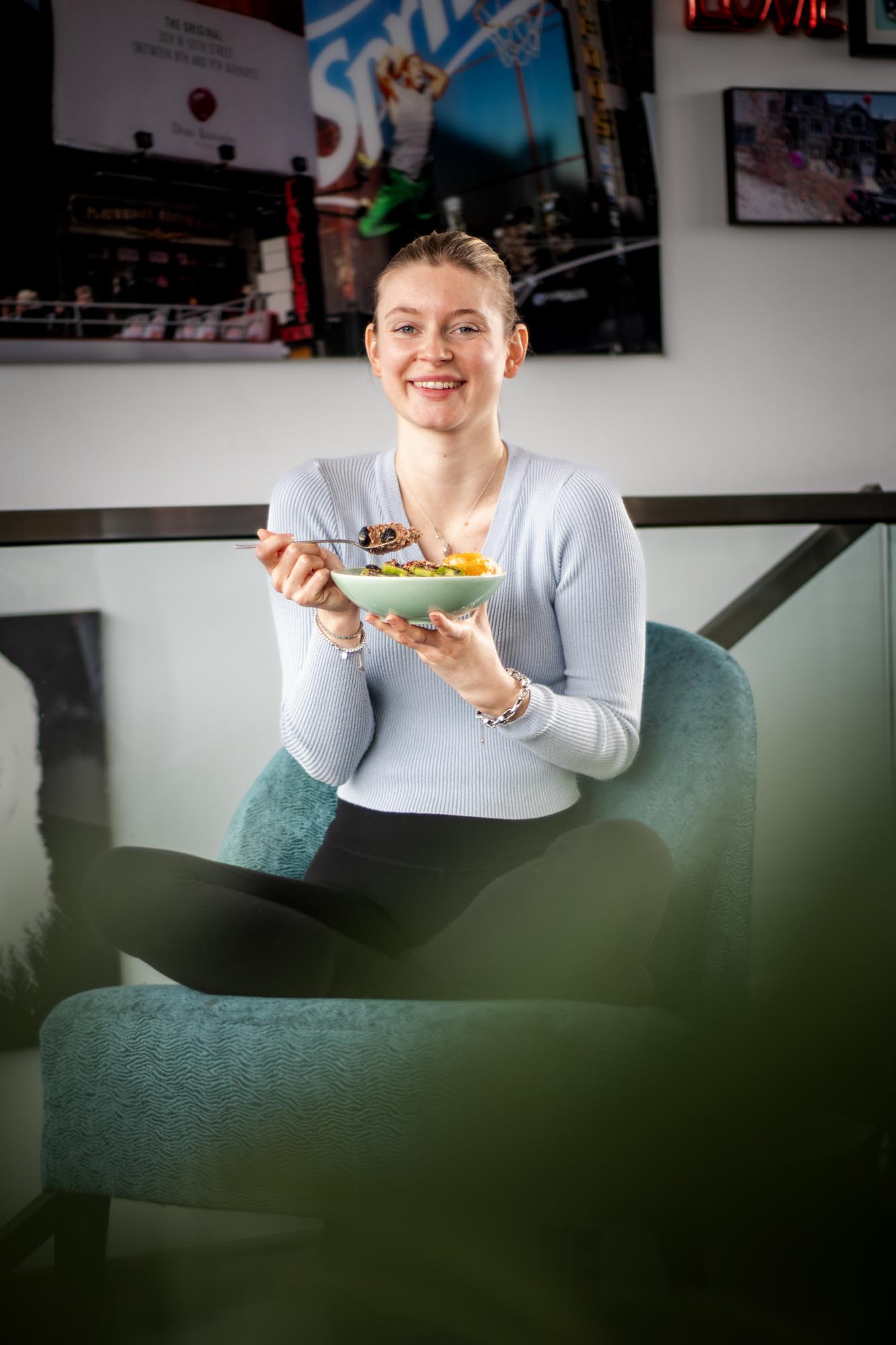 Frau sitzt auf Sofa mit Schale Frühstücksbowl in der Hand, Blick zur Seite