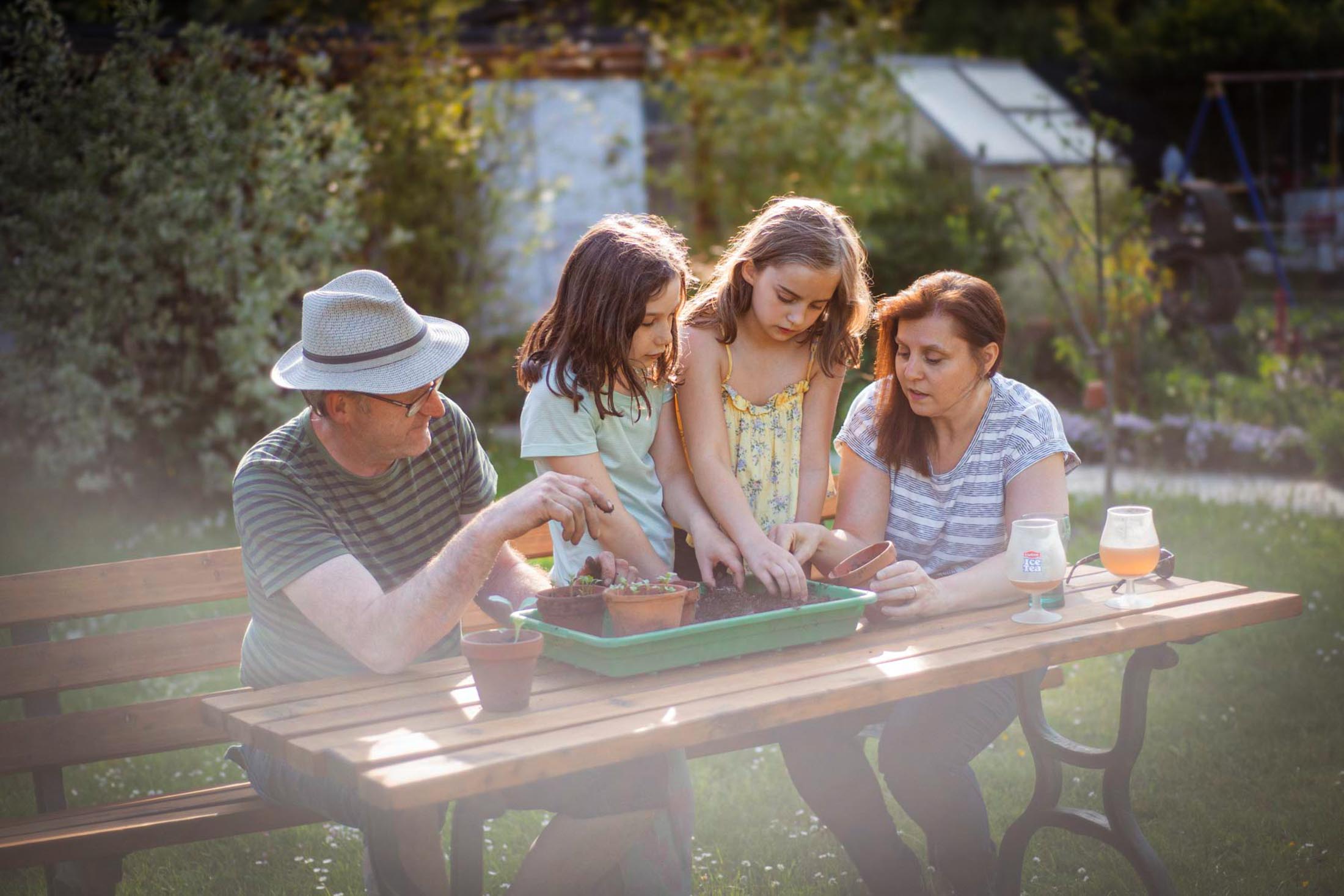 Familie sitzt am Gartentisch und beschäftigt sich gemeinsam mit Pflanzen