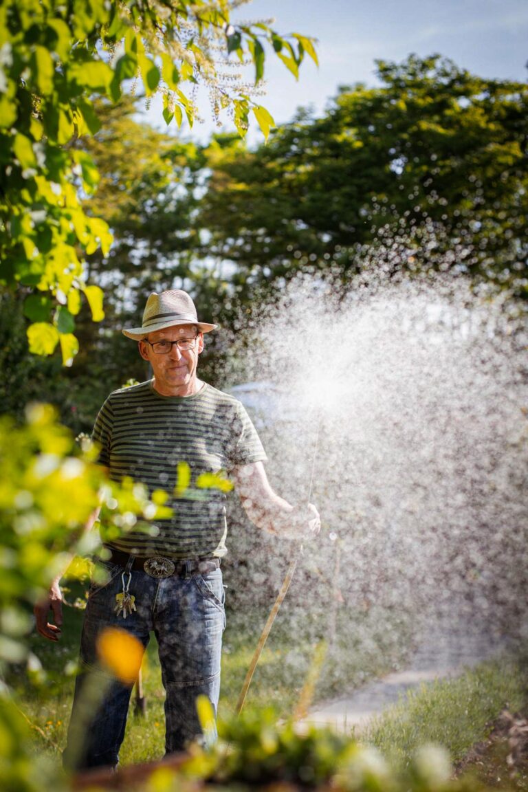 Mann gießt Pflanzen mit starkem Wasserstrahl