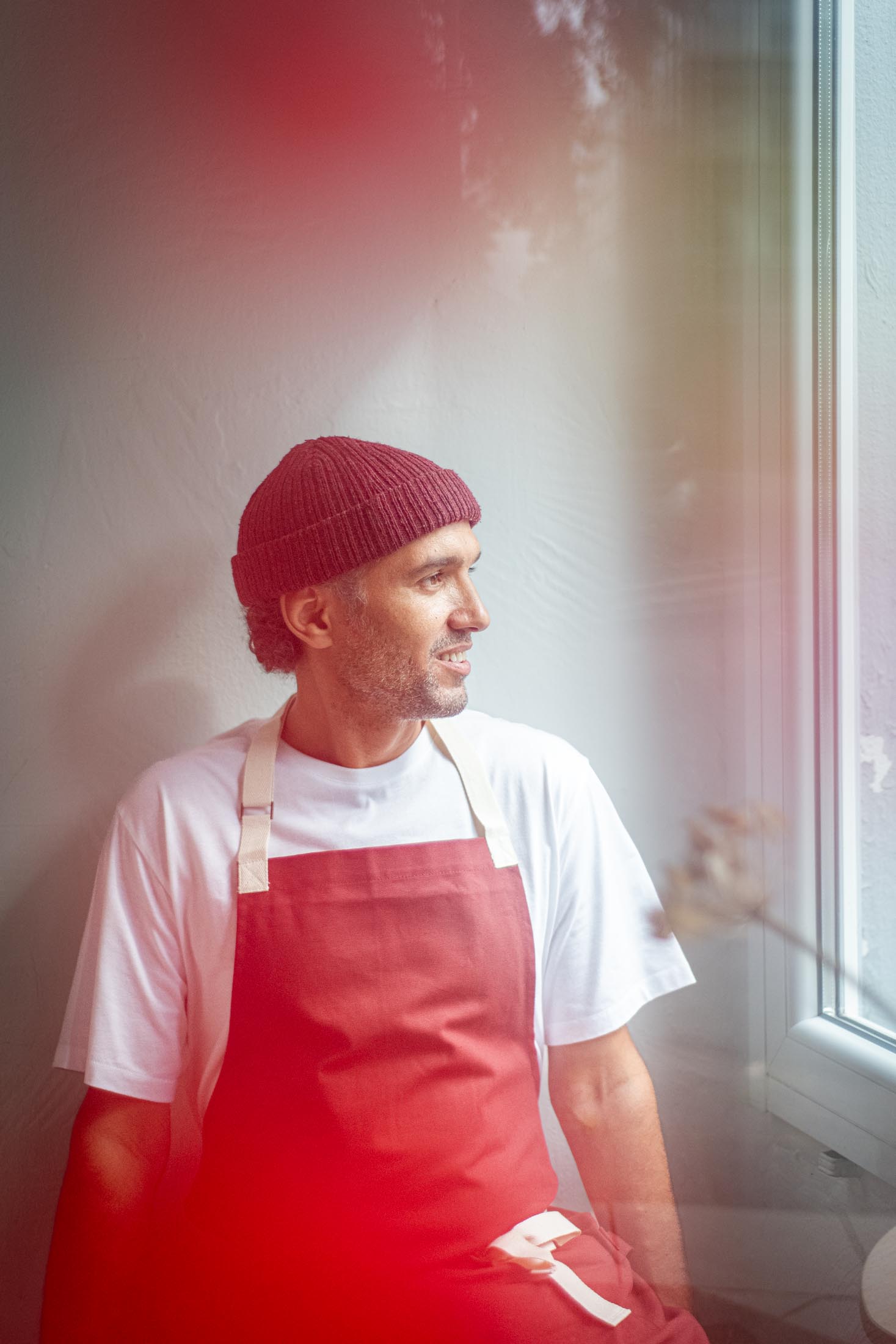 Portrait einer Person mit roter Schürze und Blick zur Seite vor hellem Hintergrund