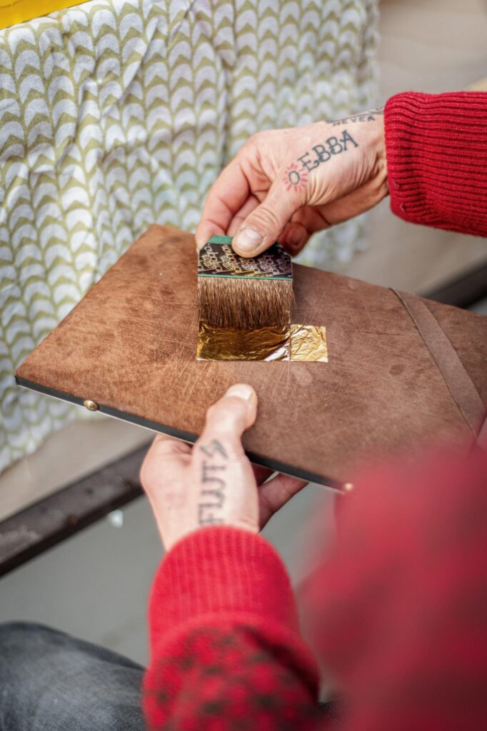 Hand nimmt mit Pinsel Blattgold von einem Holzbrett auf
