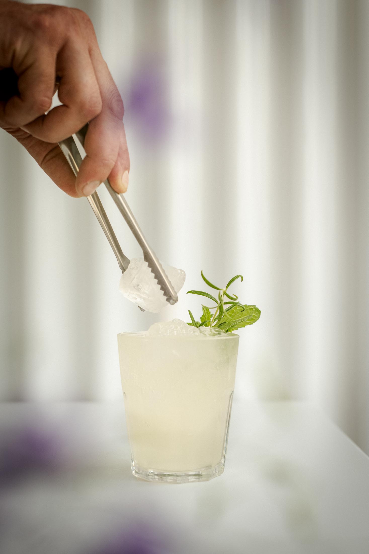 Hand setzt mit einer Pinzette Eis in ein Limonadenglas