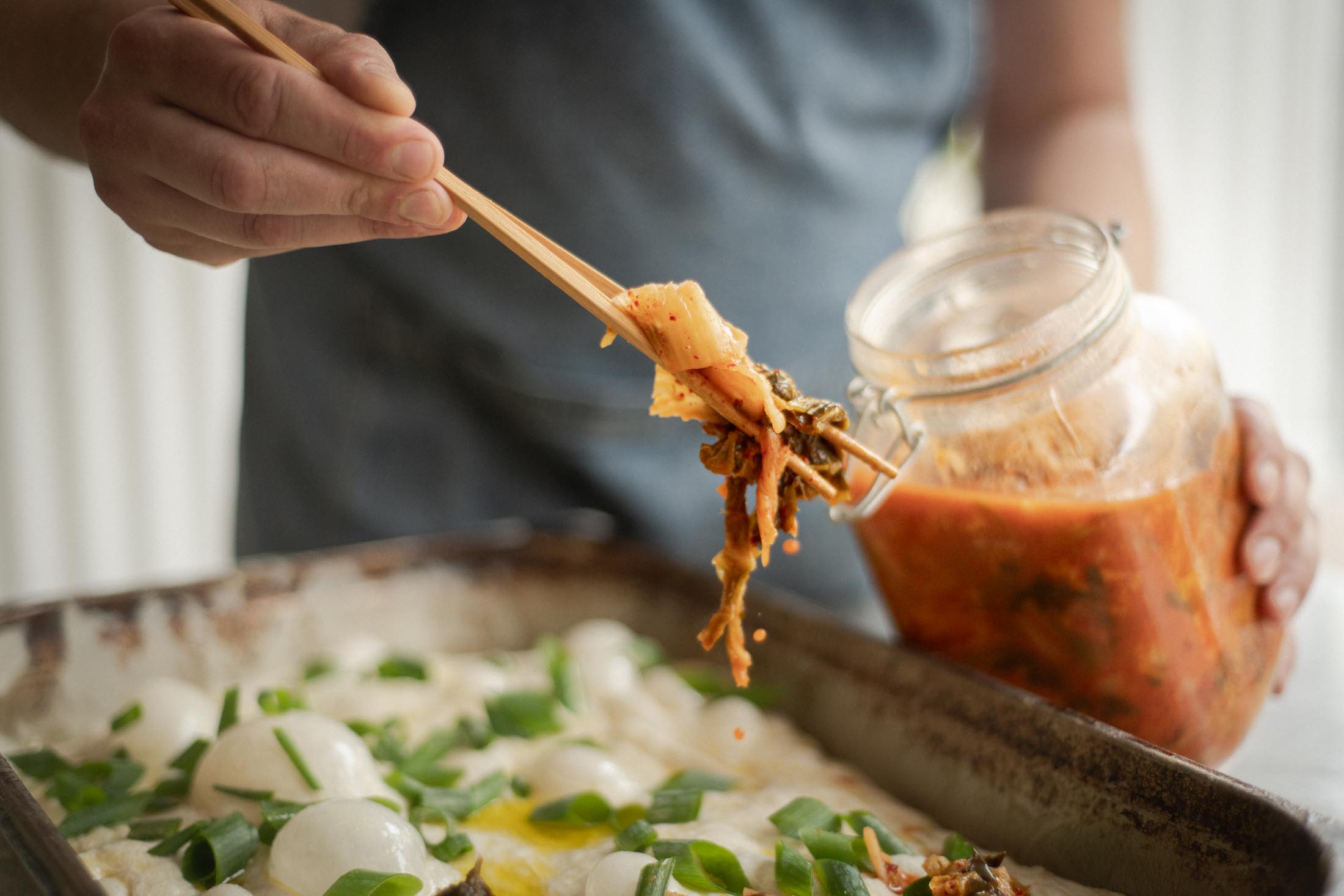 Hand gibt mit einem Löffel Kimchi aus einem Glas auf einen Teigboden