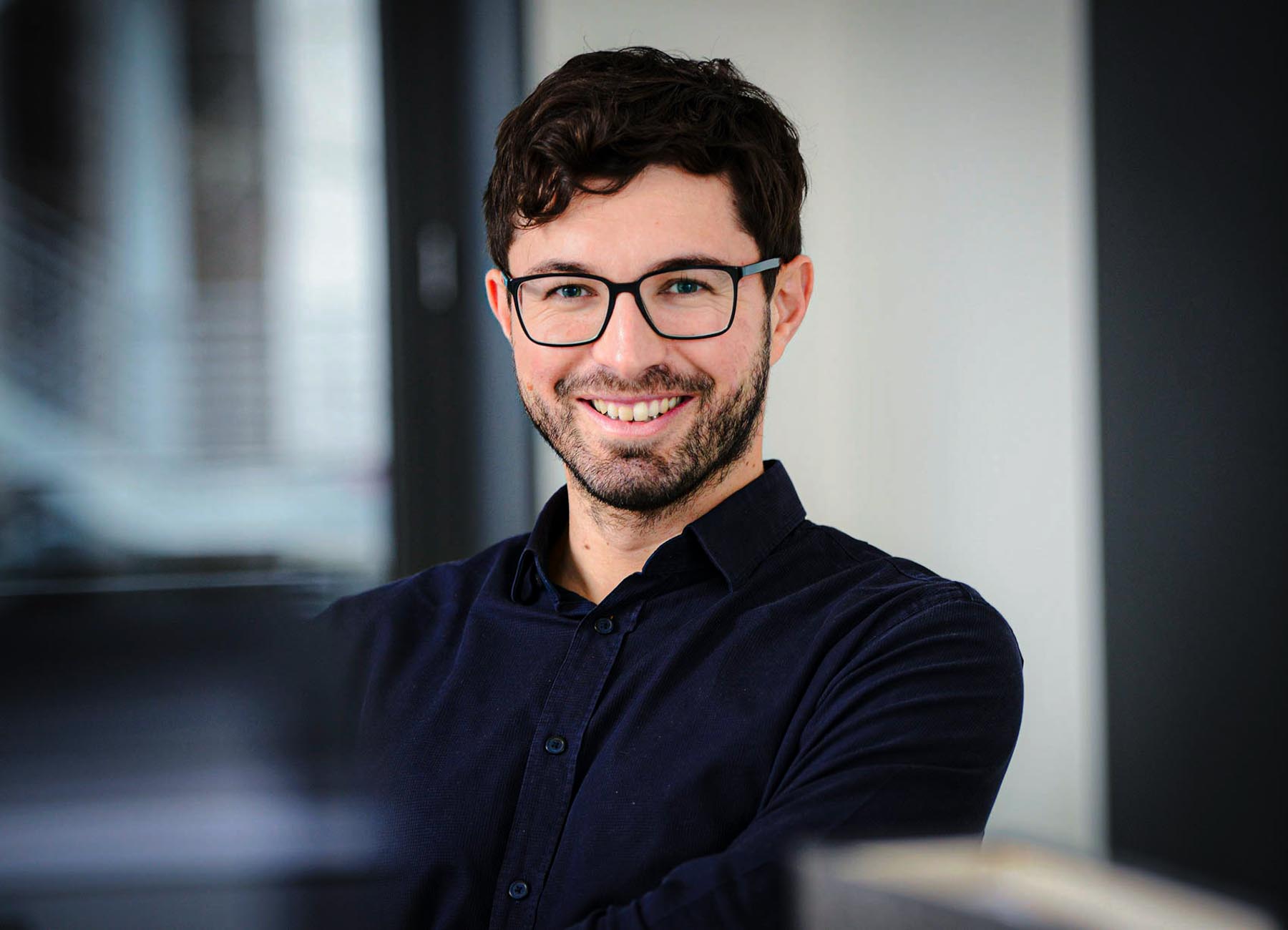 Businessportrait: Mann mit Brille vor dunklem Hintergrund, leichtes Lächeln