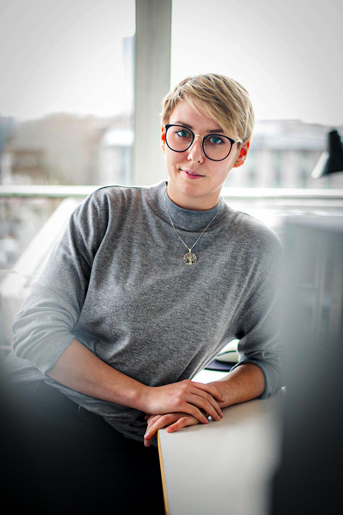 Frau mit Kurzhaarschnitt und Brille am Tisch, helles Fensterlicht