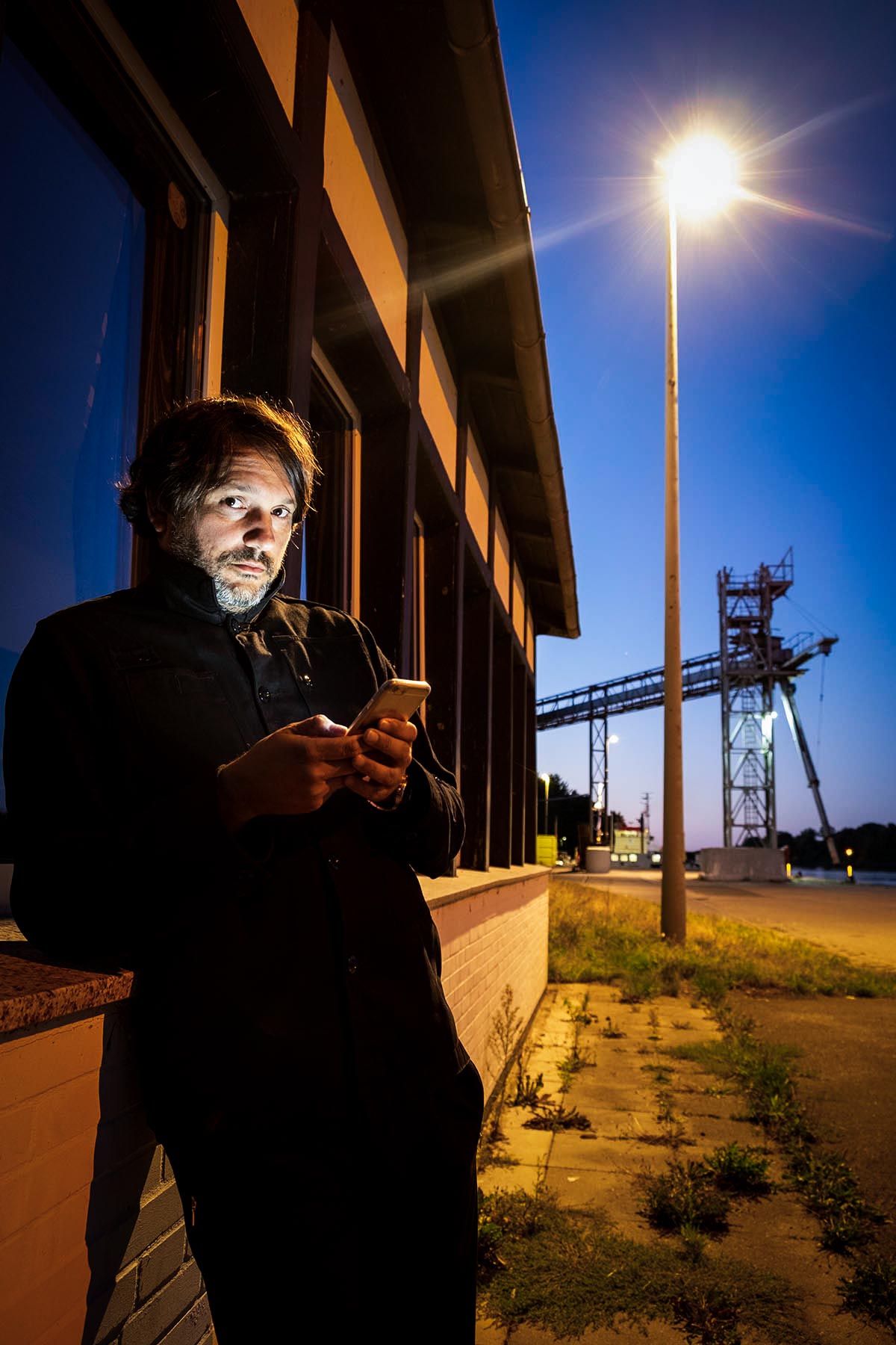 Mann im abendlichen industriellen Setting mit Handy in der Hand
