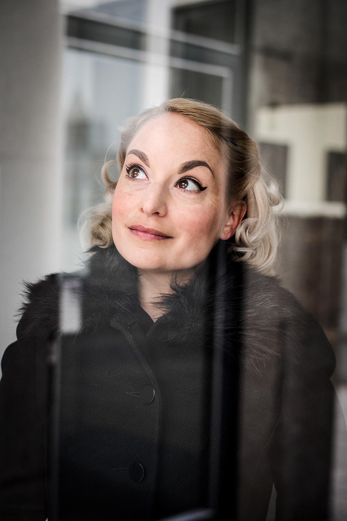 Frau im schwarzen Mantel am Fenster, Blick nach oben