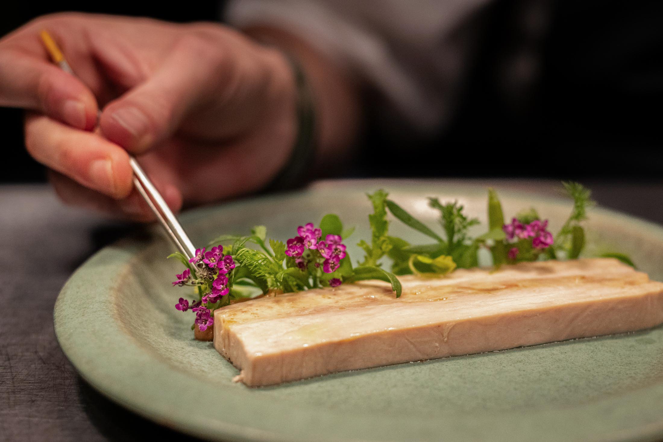 Längliches Gericht mit Kräutern und Blüten, präzise angerichtet