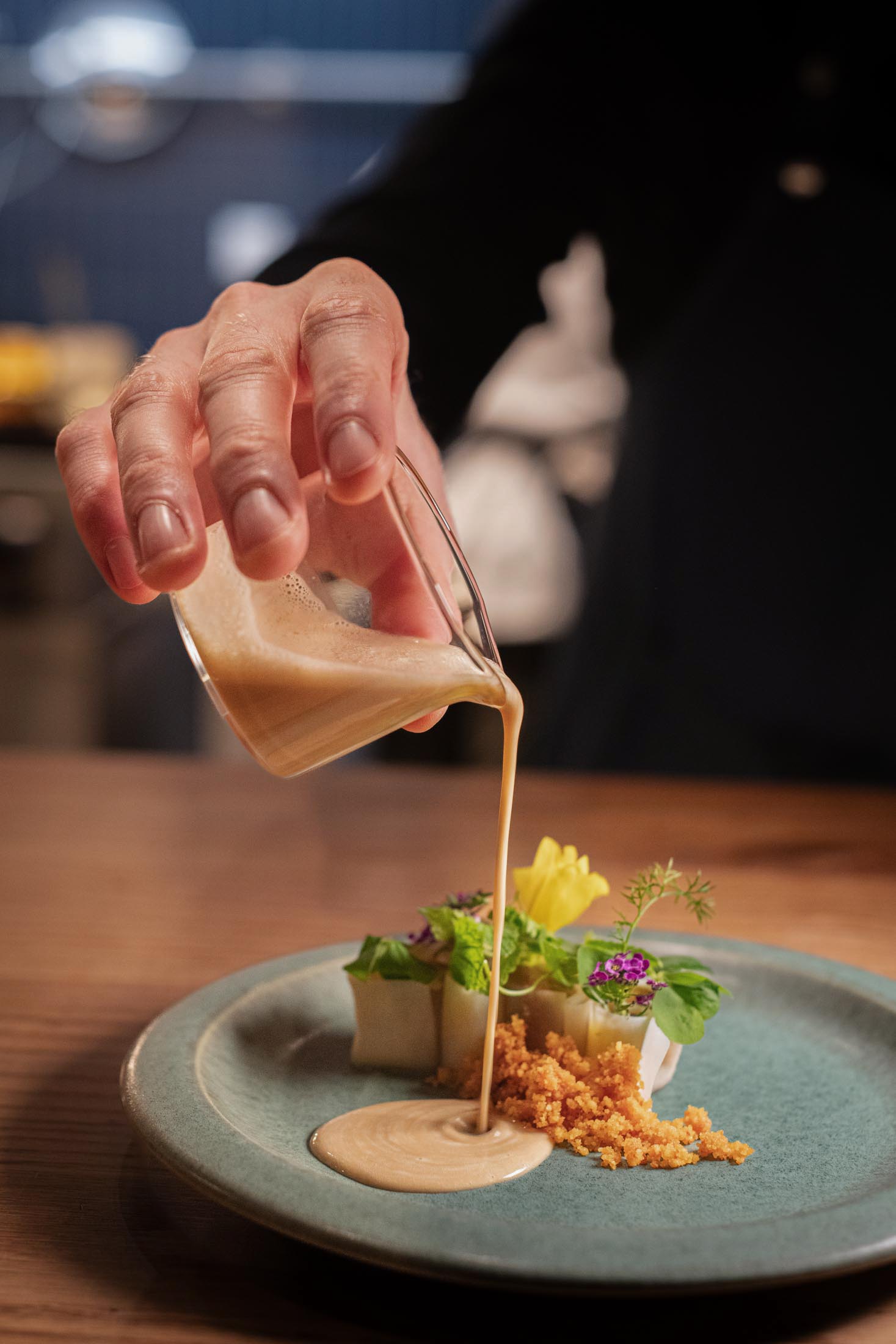 Sauce wird aus Glasgefäß über ein angerichtetes Tellergericht gegossen